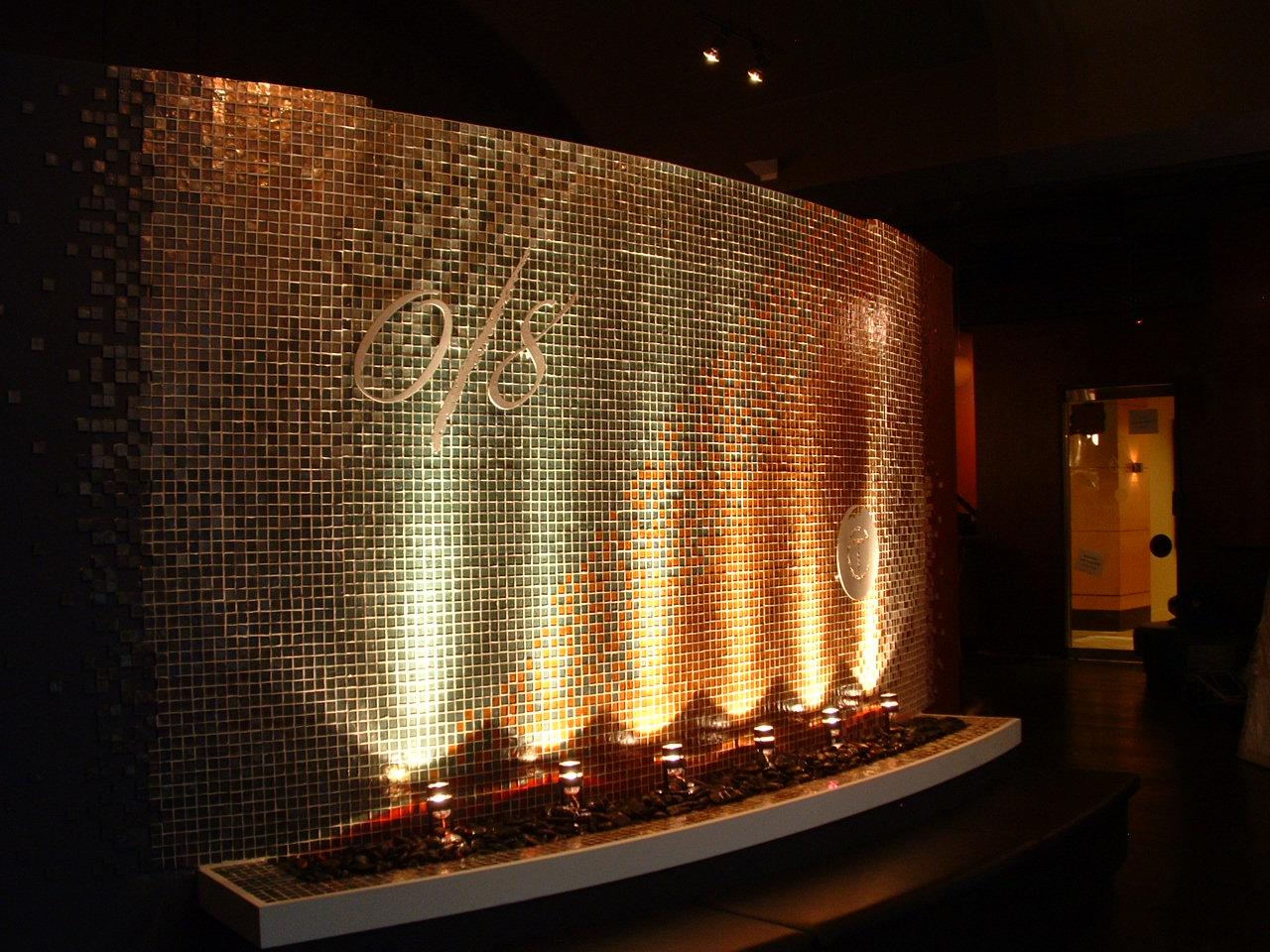 0/8 seafood grills and twisted cork wine bar located within the Bellevue WA Hyatt hotel for locally famous chef Dan Thiessen. 18 ft x 8 ft tall radius, ambiente 1 in x 1 in gradient mosaic tiles grouted into place. Pewter finished 0/8 and twisted cork stainless steel logos displayed out in front the water, infinity style hidden delivery system to add mystery, basin topped with black beach rock, up lit for a dramatic effect auto filler easy drain new construction.